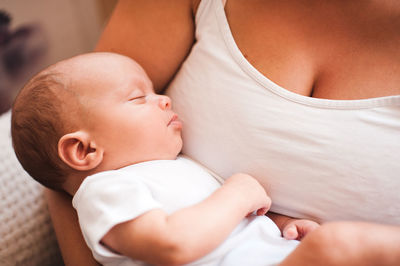 Midsection of mother holding baby boy lying at home