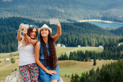 Friends talking selfie while leaning on rock against landscape