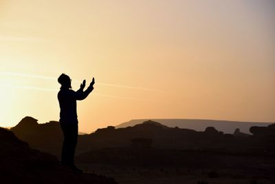 Silhouette man standing on mountain against sky during sunset