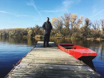 Man standing on jetty by red boat in lake against sky