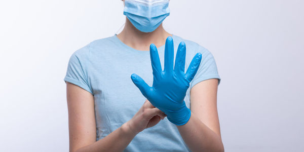 Midsection of doctor in mask wearing surgical glove against gray background
