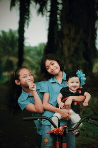 Portrait of happy sisters with bicycle at park