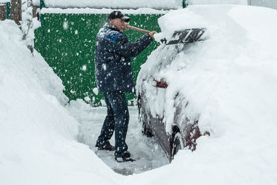A man in a cap is shoveling snow off a car that was covered in snow during the snowfall