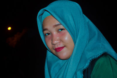 Portrait of smiling young woman wearing hijab at night