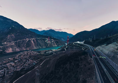 Bridge over river amidst mountains against sky during sunset