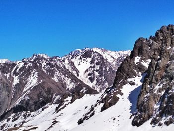 Low angle view of snowcapped mountains against clear blue sky