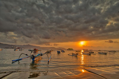 Boats moored on sea against cloudy sky during sunset