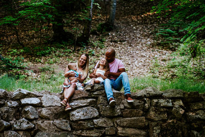 Happy multiracial family laughing while sitting on rocks in forest