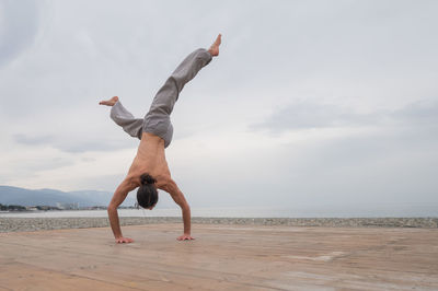 Rear view of woman jumping at beach against sky