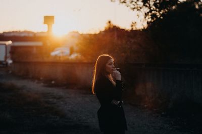 Side view of young woman standing against sunset