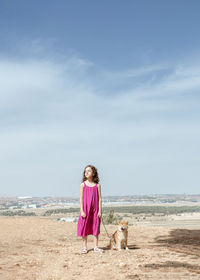 Little girl in dress standing with cute obedient purebred shiba inu dog on hill while spending summer day together in countryside