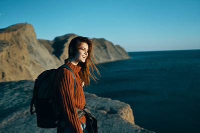 Woman standing on rock at sea against sky