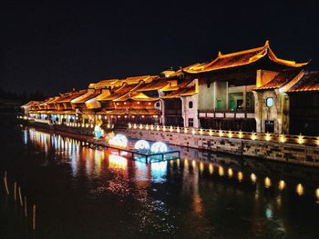 Illuminated buildings by river against sky at night