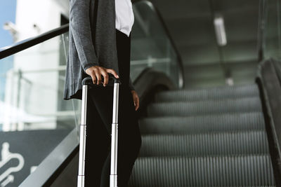 Midsection of woman holding luggage while standing on escalator