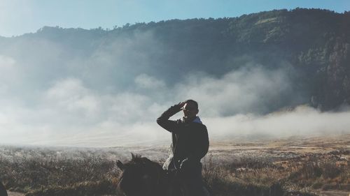 Man saluting while sitting on horse against mountains during foggy weather