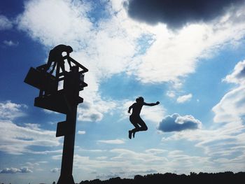 Low angle view of woman jumping against cloudy sky