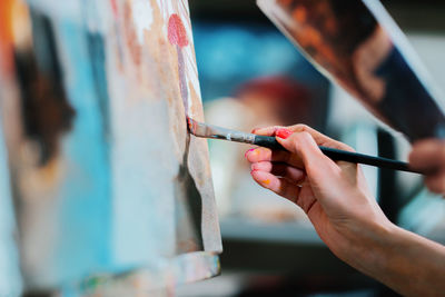 Close-up of woman hand painting on canvas in studio