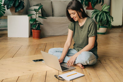 Female student sitting on the floor uses a laptop to study online.