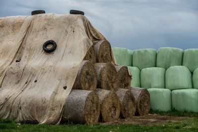 Stack of hay bales on field against sky