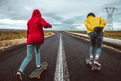 Full length of couple skateboarding on road against sky