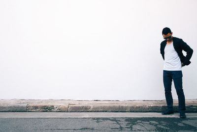 Young man looking down standing against white wall