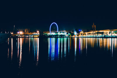 Illuminated city by river against sky at night