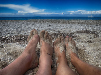 Low section of people on beach against sky