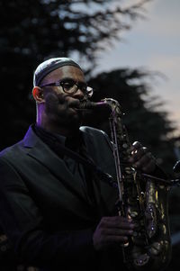 Man playing musical instrument standing against trees at night