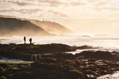 People standing on rock by sea against sky