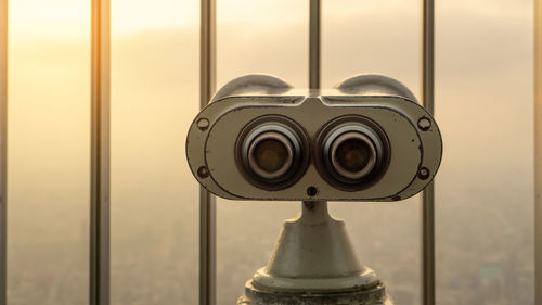 Close-up of coin-operated binoculars against sky seen through window