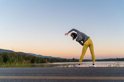 Back view of a woman stretching her arms and legs before her morning exercise at a local lake park