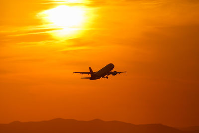 Silhouette airplane flying against orange sky