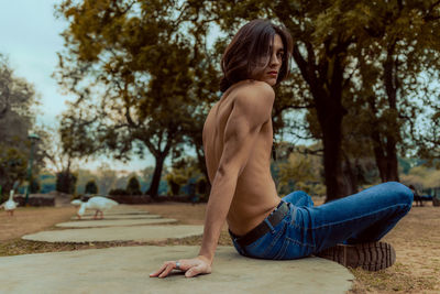 Portrait of shirtless man sitting on footpath in park