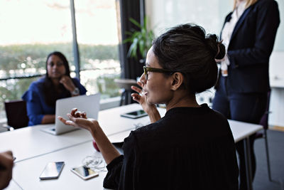 Businesswoman gesturing while discussing with colleagues during meeting at conference table in board room