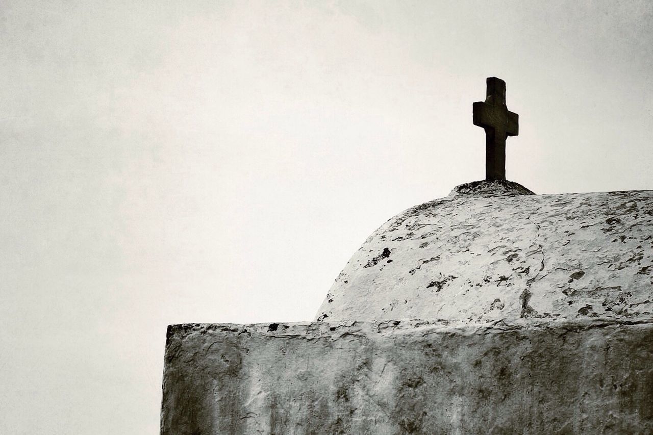 low angle view, clear sky, copy space, architecture, built structure, building exterior, cross, wall - building feature, religion, high section, spirituality, wall, sky, day, outdoors, stone wall, no people, protection, old