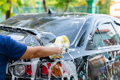 Woman hand hold yellow sponge washing spoiler black car at home. car detailing.
