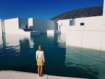 Rear view of woman standing at lake against sky