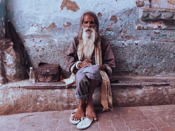 Full length portrait of a man sitting against wall