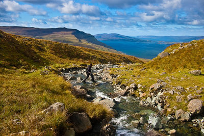 Man crossing stream against sky