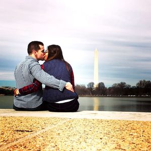 Rear view of couple kissing by reflection lake against washington monument