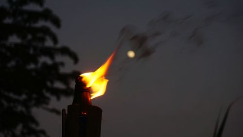 Close-up of burning candle against sky at night