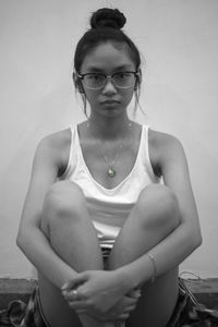 Portrait of young woman sitting against wall