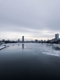 Buildings by river against sky in city during winter