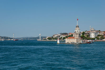 Sailboats in sea by buildings against clear sky