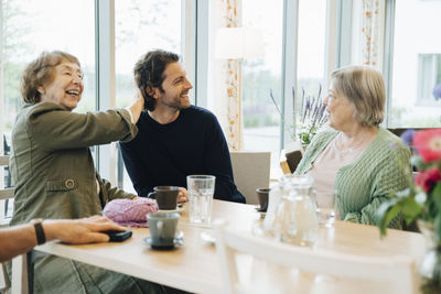 Smiling man sitting amidst senior women at dining table in retirement home