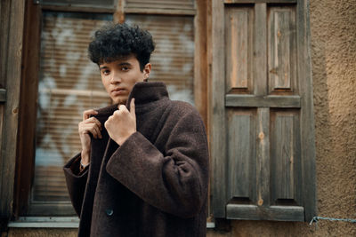 Young man looking away while standing against wall