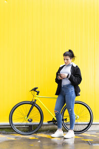 Full length of man holding bicycle against yellow wall