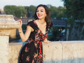 Portrait of smiling young woman standing against retaining wall
