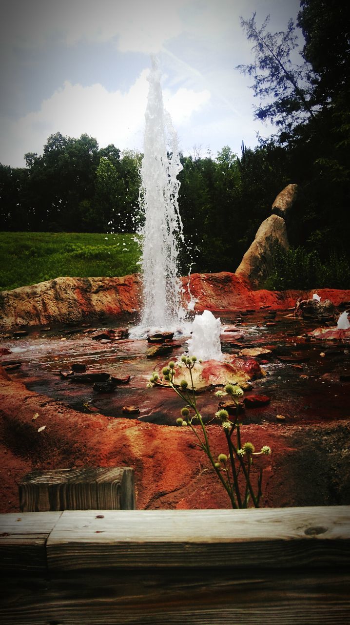 tree, building exterior, built structure, fountain, motion, architecture, waterfall, flowing water, long exposure, sky, splashing, day, outdoors, nature, water, park - man made space, blurred motion, plant, spraying, house