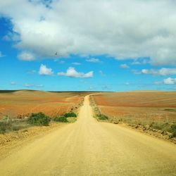 Dirt road passing through landscape against cloudy sky